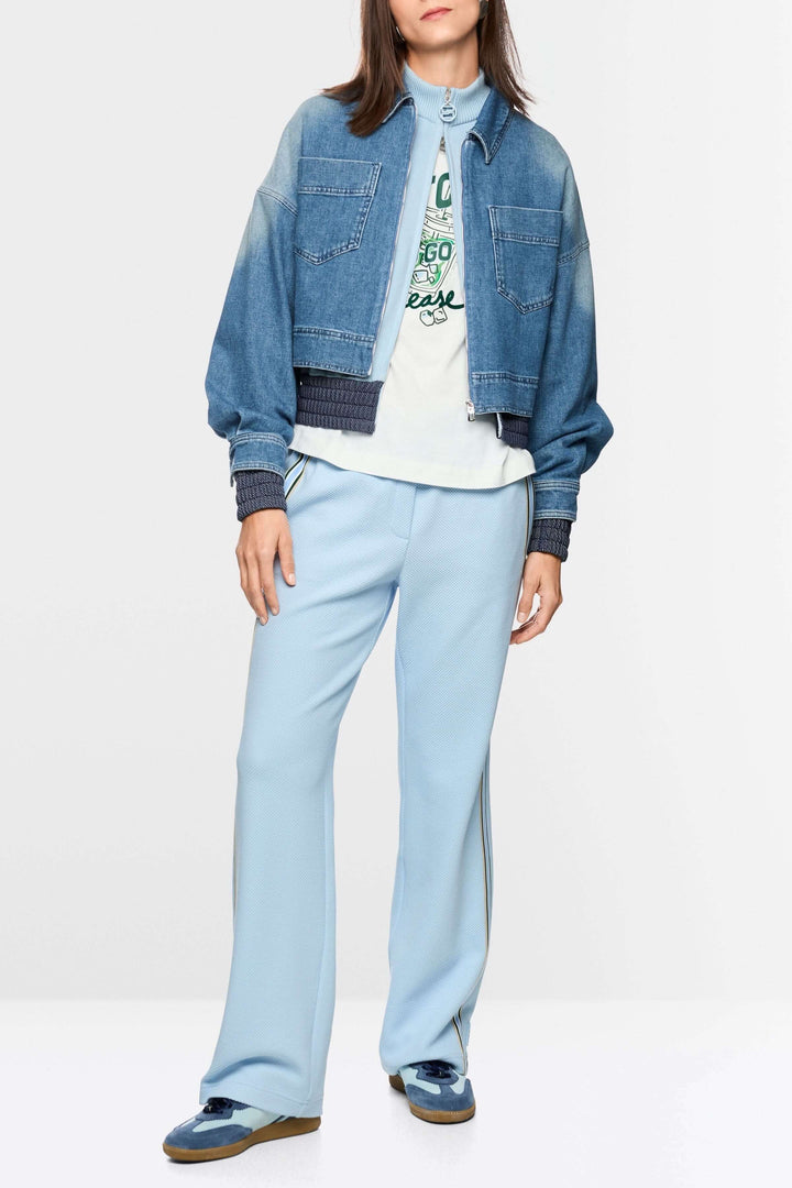 Femme portant une veste courte en jean avec fermeture éclair, coupe ample, denim souple, poches plaquées, esprit utilitaire et confort optimal.