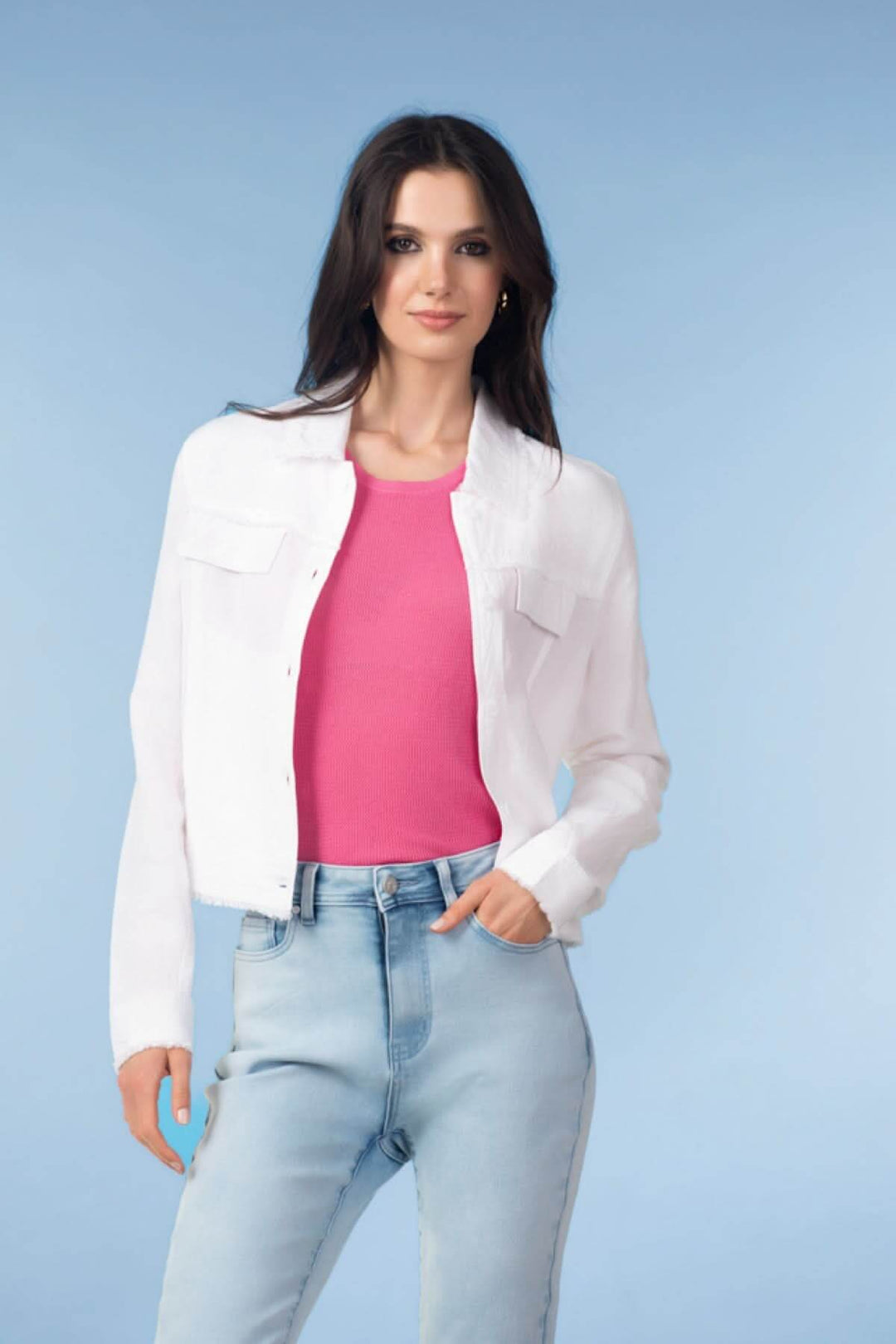 Femme portant une veste courte à finitions effilochées, avec un haut rose et un jean clair.