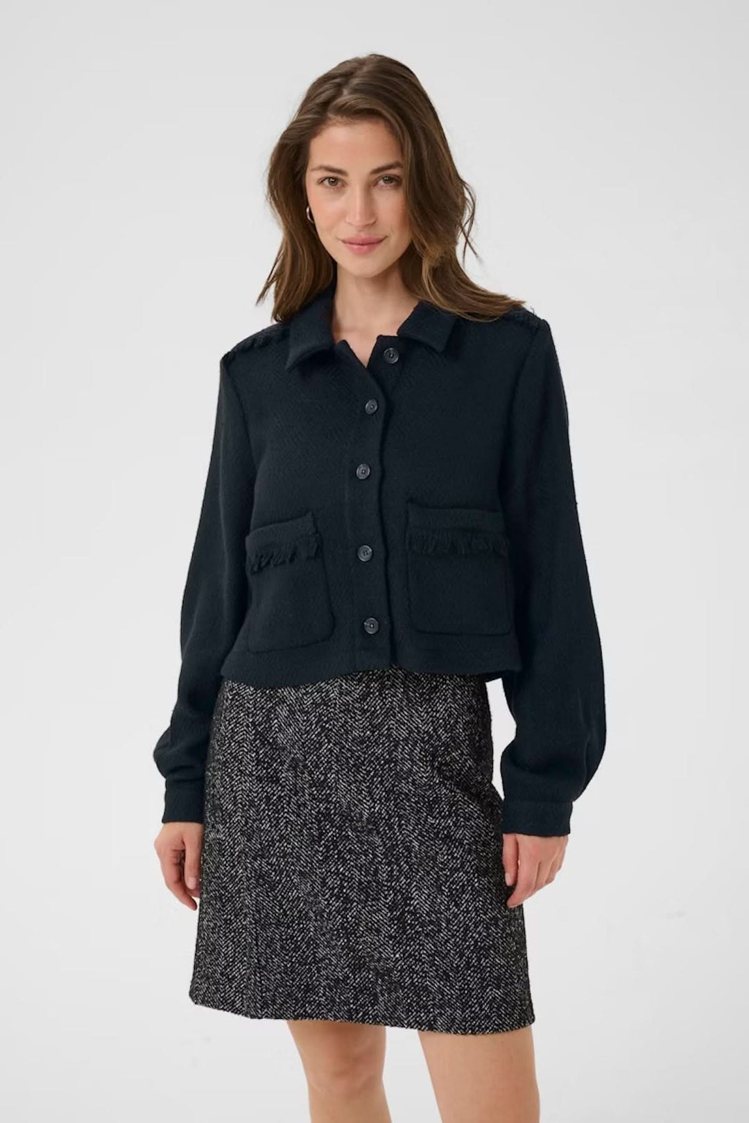 Veste décontractée noire à col chemise, poches avec franges, portée avec une jupe élégante.