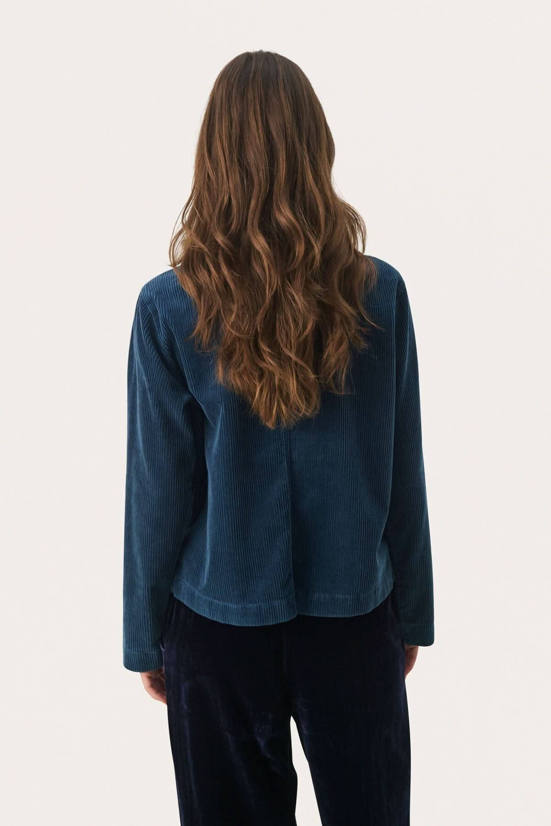 Modèle vue de dos portant une veste en corduroy de couleur bleu foncé, avec des cheveux longs et ondulés.