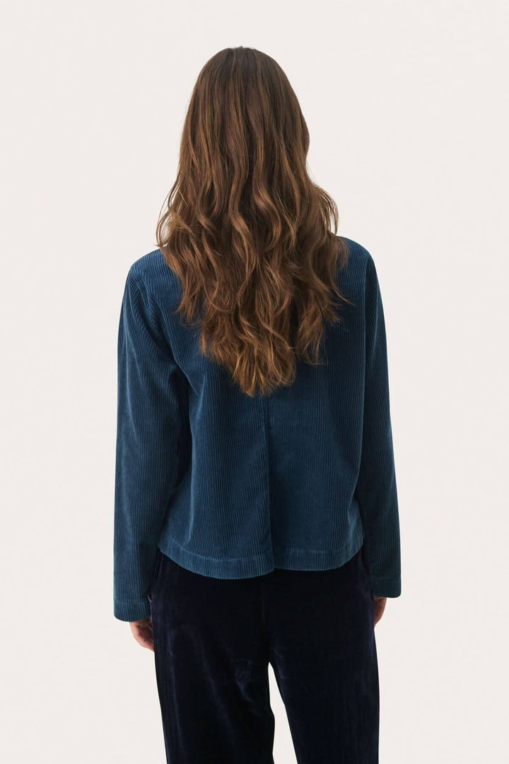 Modèle vue de dos portant une veste en corduroy de couleur bleu foncé, avec des cheveux longs et ondulés.