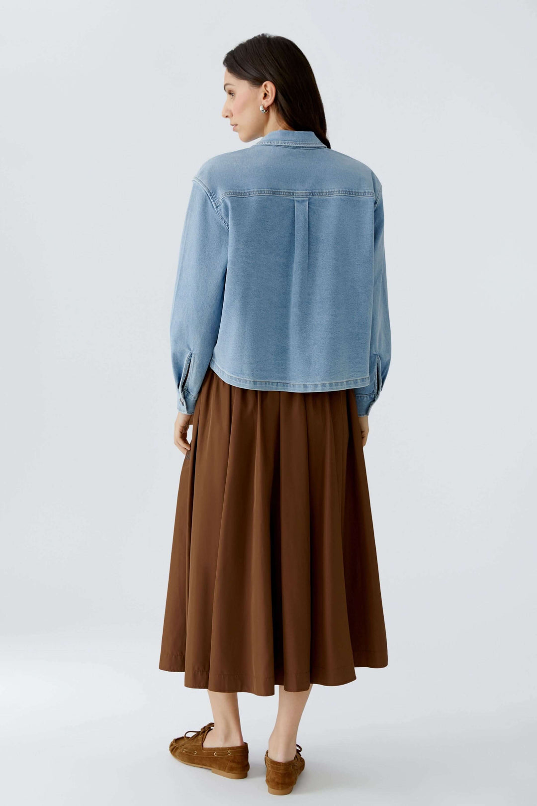 Femme portant une veste en denim avec coupe droite légèrement ample, vue de dos, superposée à une tenue décontractée.