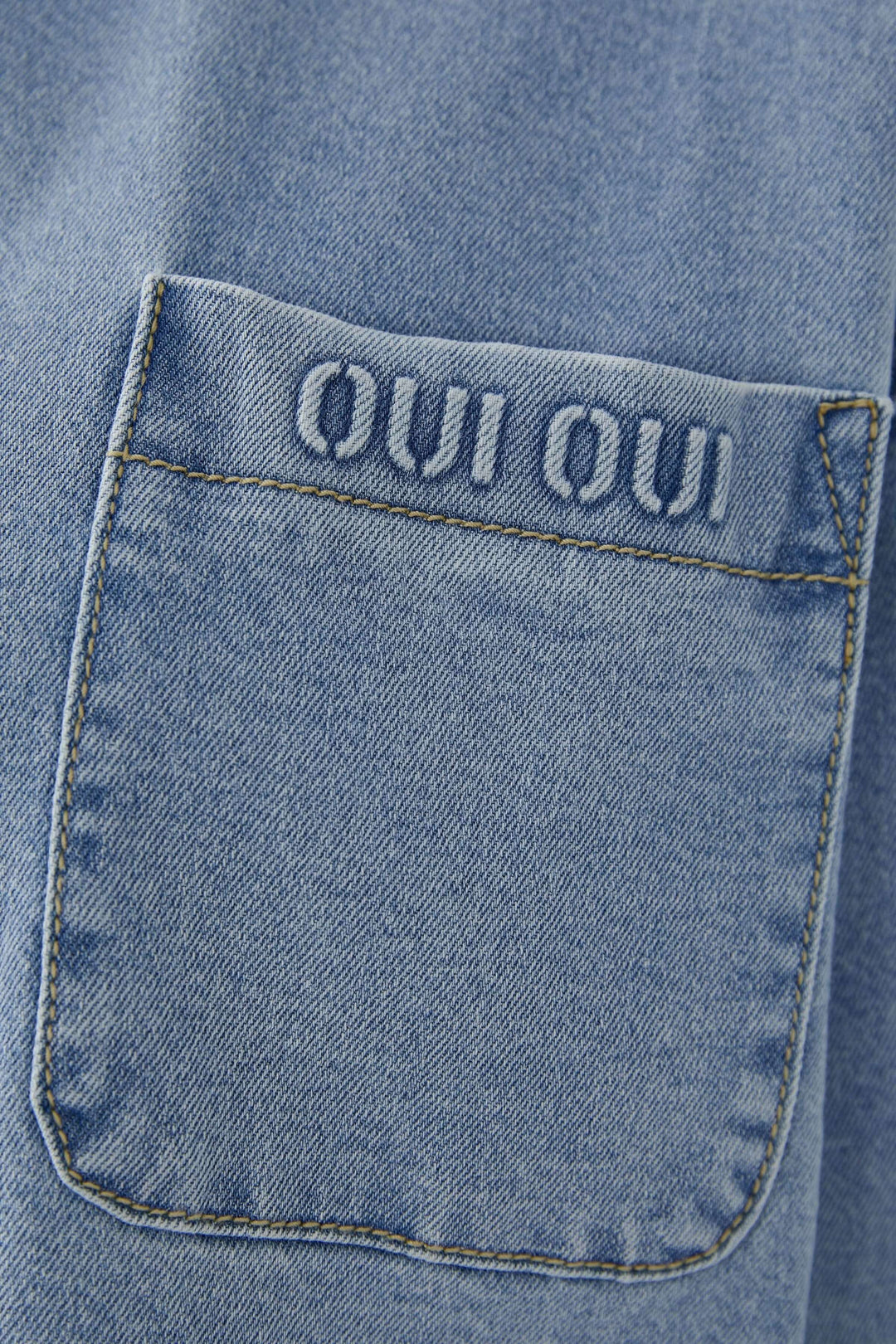 Vue de détail d'une veste en denim avec une poche brodée 'OUI OUI', ajoutant une touche unique et moderne.