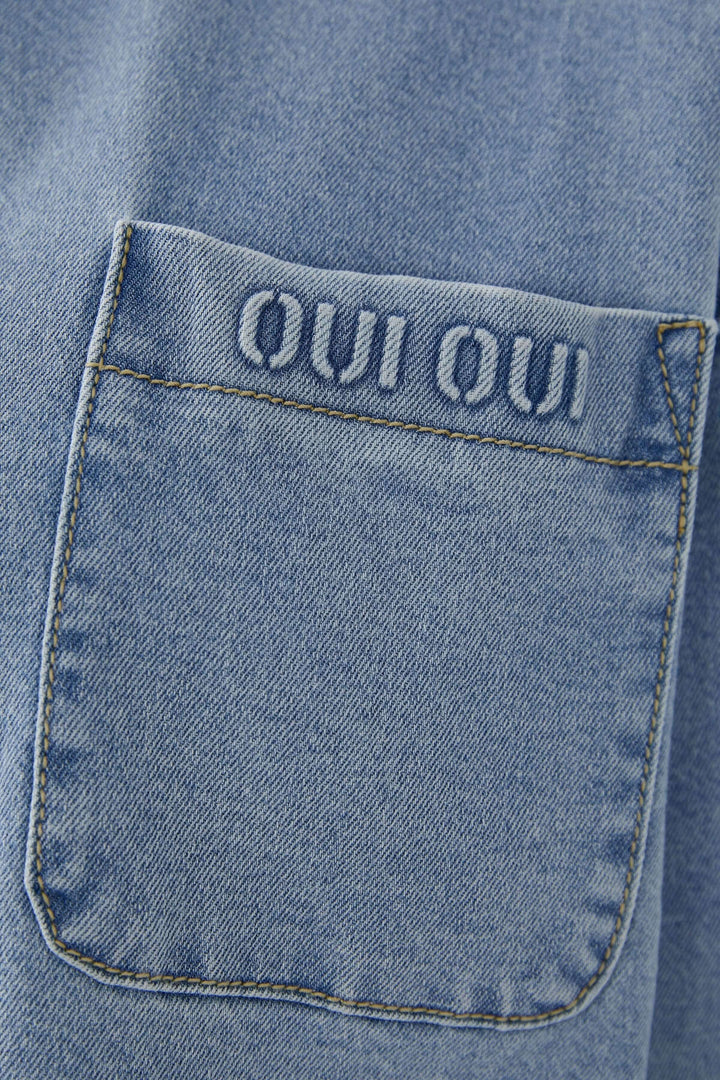 Vue de détail d'une veste en denim avec une poche brodée 'OUI OUI', ajoutant une touche unique et moderne.
