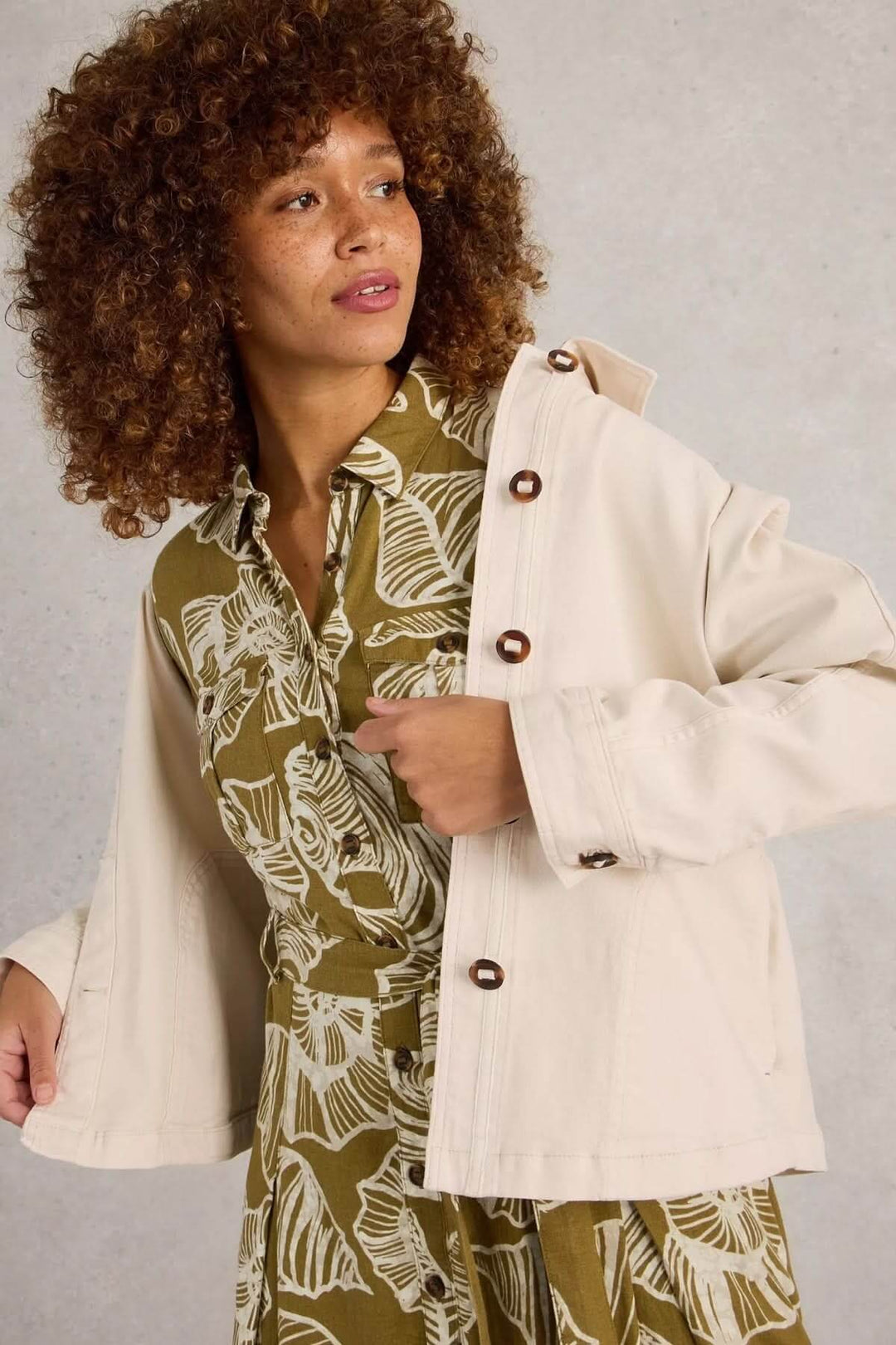 Femme portant la Veste en denim Eden à col, coupe droite, sur une robe imprimée, dans un cadre décontracté et élégant.