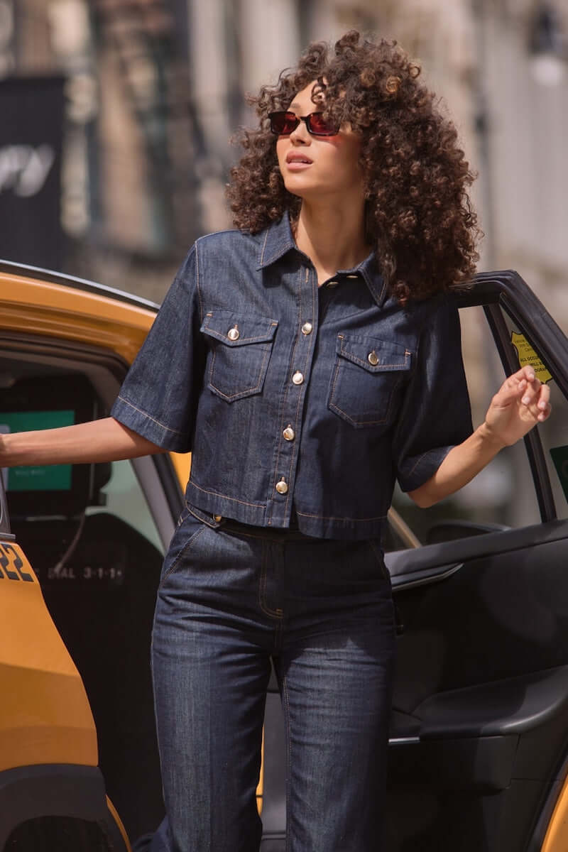 Veste en jean courte à manches évasées, portée avec un look casual-chic devant un taxi.