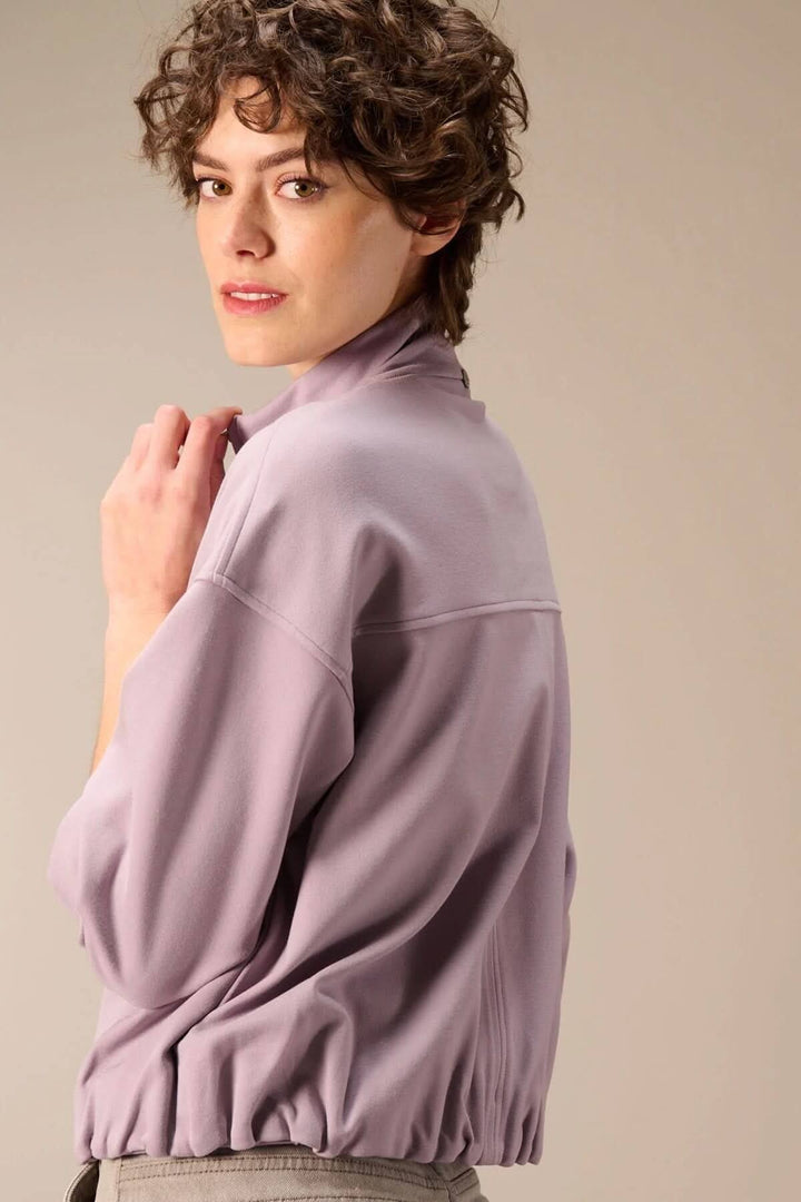 Veste en sweat avec fermeture éclair dans une teinte lavande portée par une personne, mettant en valeur un col montant et une coupe ample.