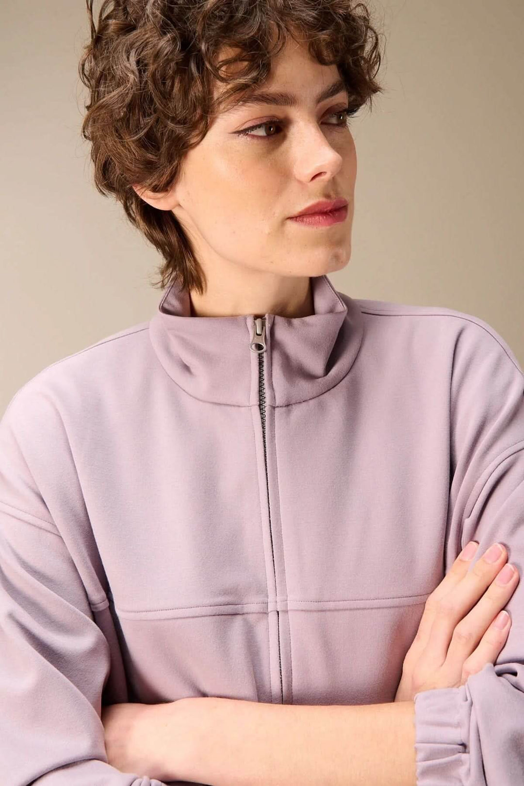 Femme portant une veste en sweat avec fermeture éclair mauve, col montant structuré, style décontracté, idéale pour une tenue casual chic.