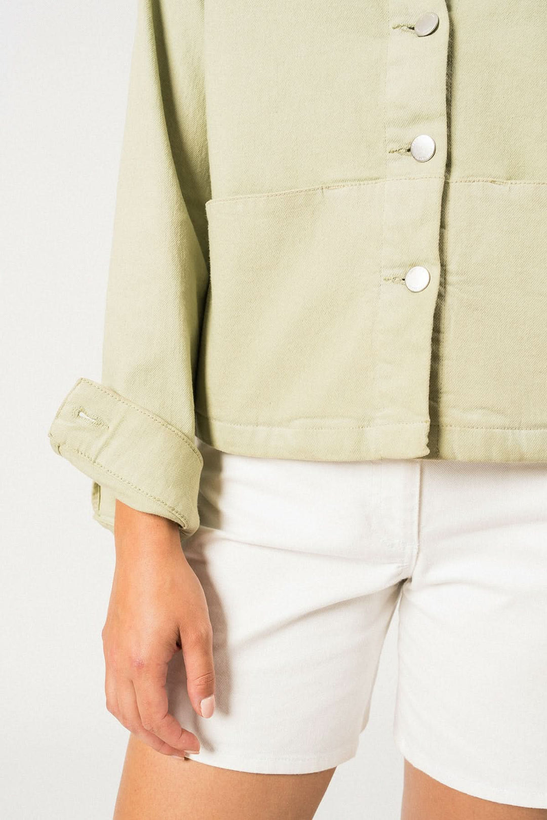 Veste en toile de coton ST TEA, coupe féminine, boutons argentés, portée avec shorts blancs.