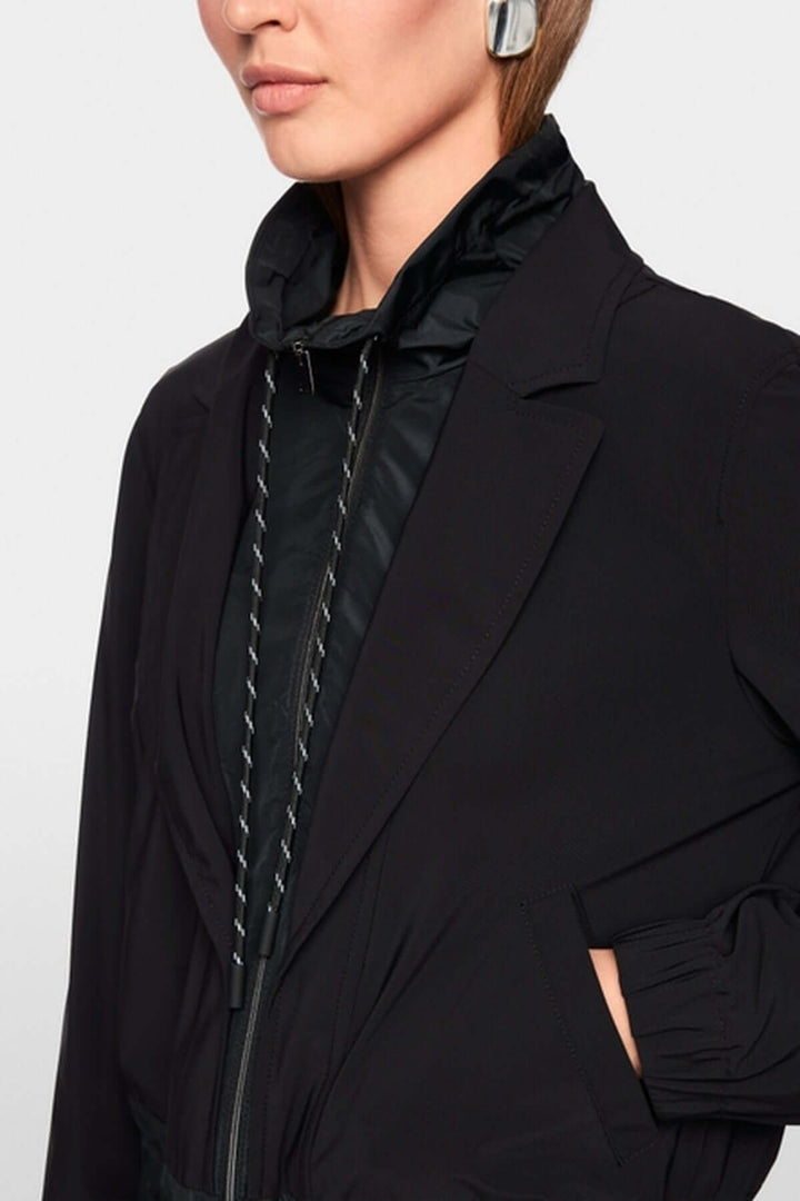 Veste légère noire avec col à revers style blazer, poignets élastiques et fermeture éclair, alliant sport et élégance.