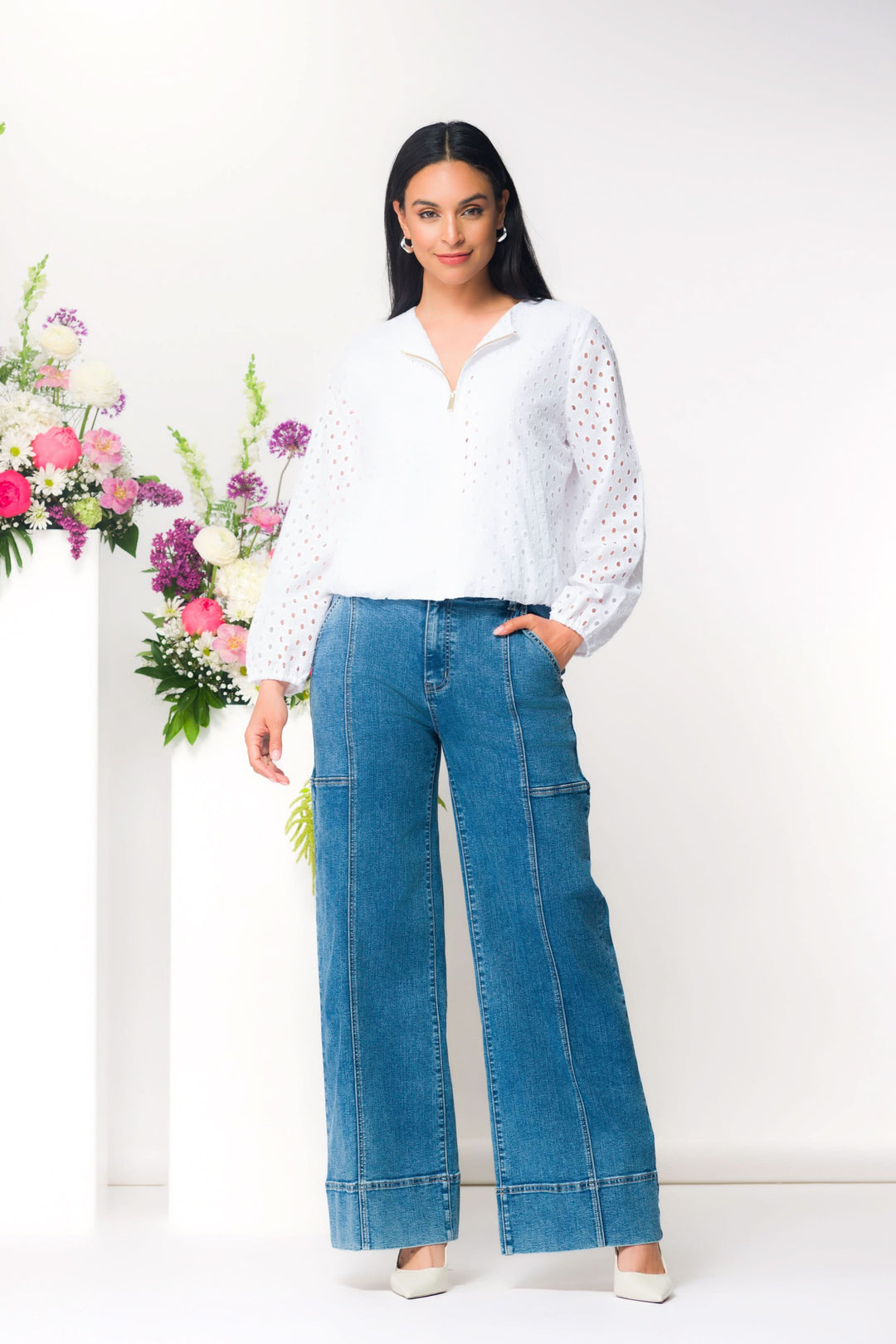 Femme portant une veste légère ajourée à fermeture zippée avec un style moderne, debout devant des fleurs colorées.