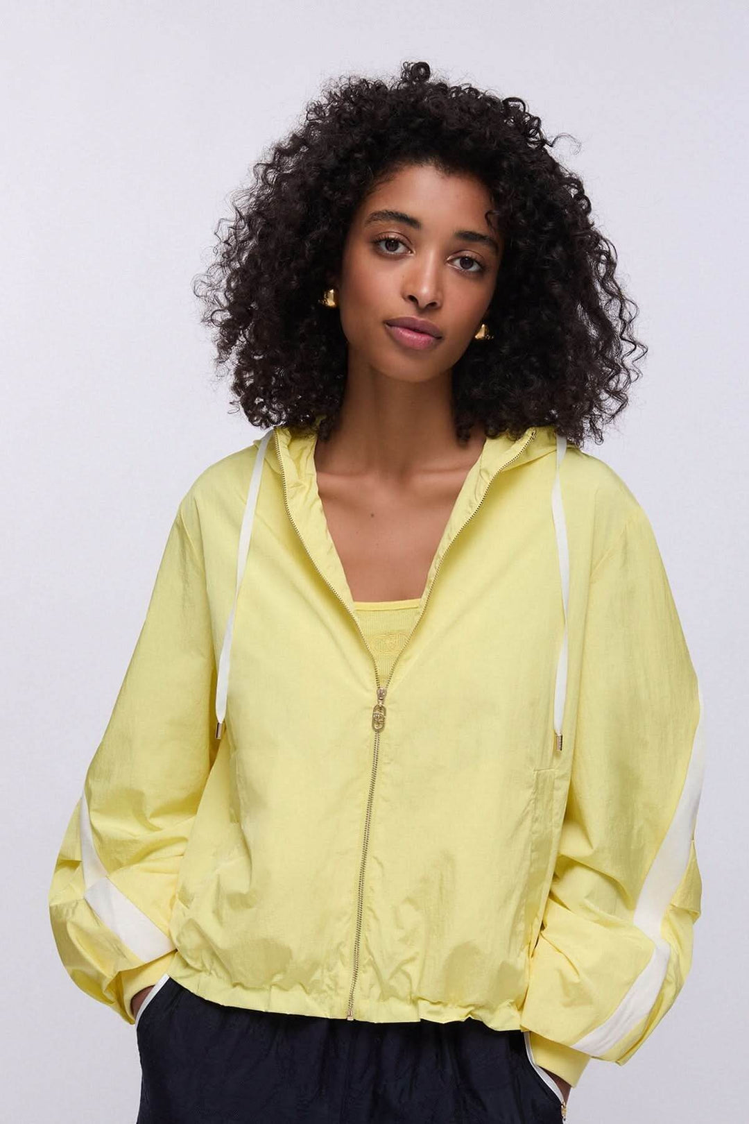 Femme portant une veste légère à capuche zippée jaune, coupe moderne et décontractée, idéale pour la mi-saison.