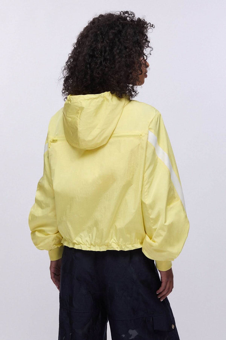 Veste légère à capuche zippée vue de dos, couleur jaune, portée par une femme sur fond blanc.
