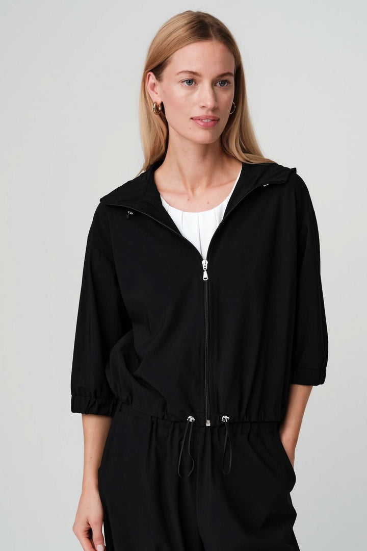 Femme portant une veste légère zippée à taille ajustable noire avec manches trois-quarts et col montant, idéal pour style sport-chic.