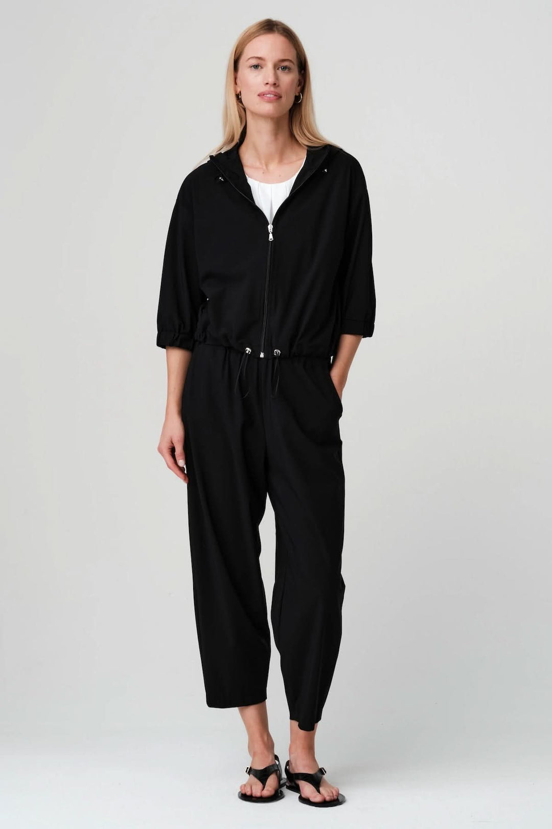 Veste légère zippée à taille ajustable, élégante et polyvalente, portée avec un ensemble noir, manches trois-quarts, fermeture éclair visible.
