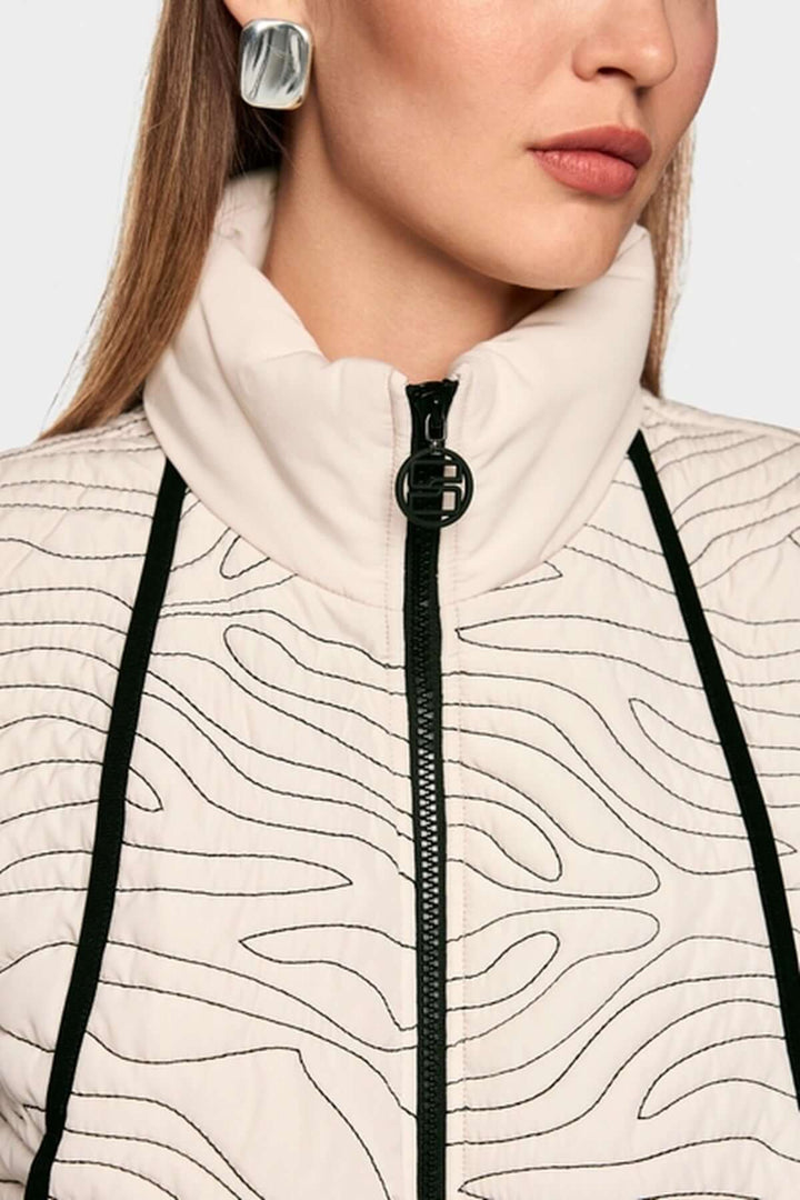 Veste matelassée avec surpiqûres ondulées, col montant, et fermeture éclair, vue de près sur les détails de couture et texture.