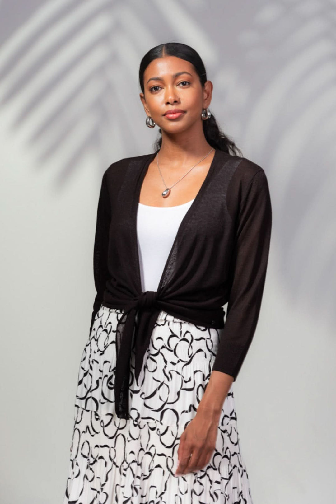 Veste ouverte légère noire nouée à la taille, portée avec un débardeur blanc et une jupe imprimée.