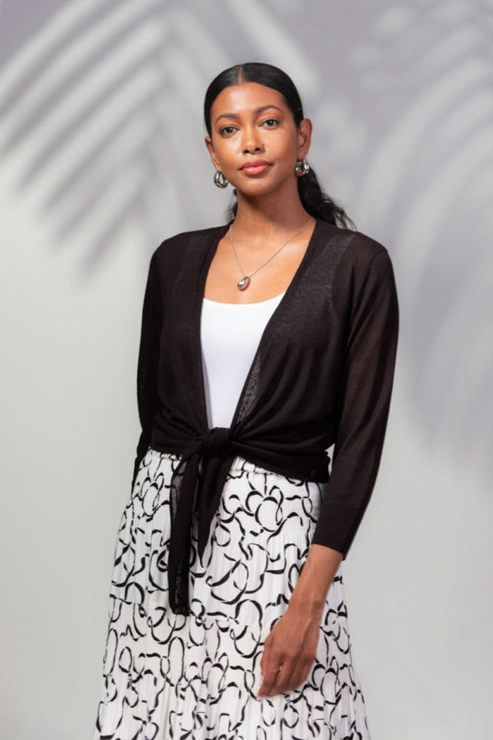 Veste ouverte légère noire nouée à la taille, portée avec un débardeur blanc et une jupe imprimée.