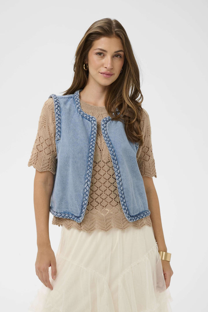 Veste sans manches Rina en denim avec bordure tressée sur modèle, design bohème moderne pour superpositions élégantes.