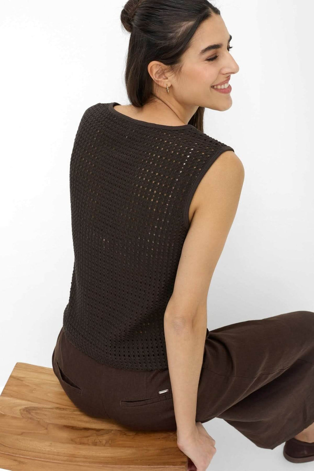 Veste sans manches ajouré INA en maille texturée sur une femme assise, offrant un style moderne et estival.