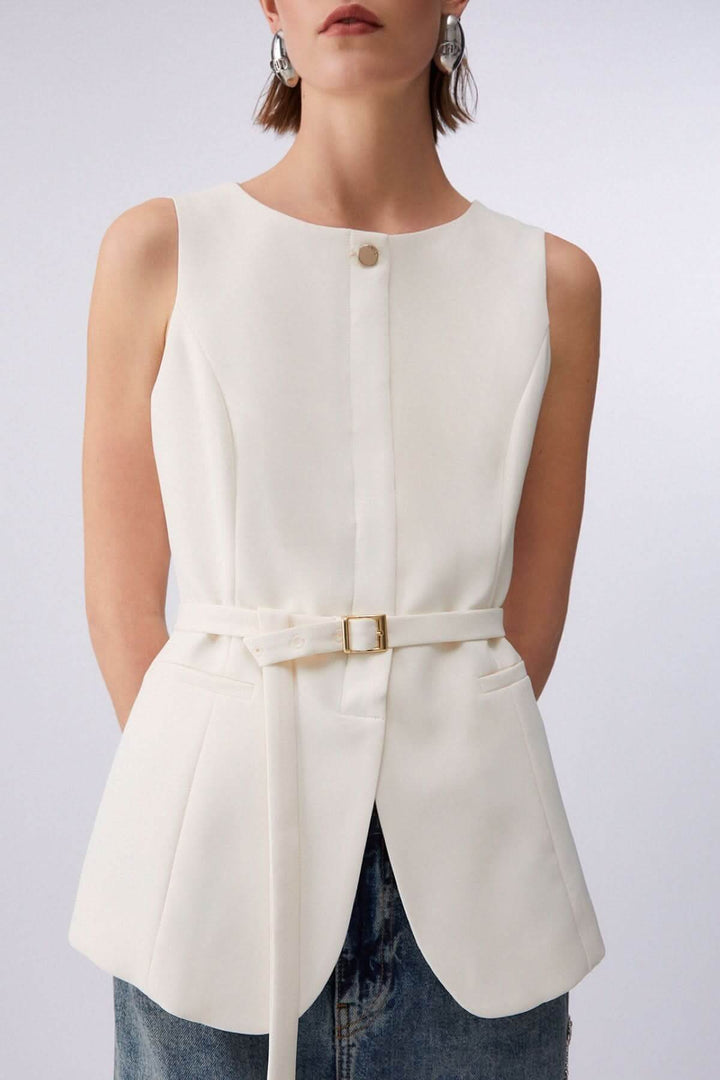 Veste sans manches avec ceinture blanche, bouton décoratif, encolure ronde, portée par une femme, design élégant et structuré.