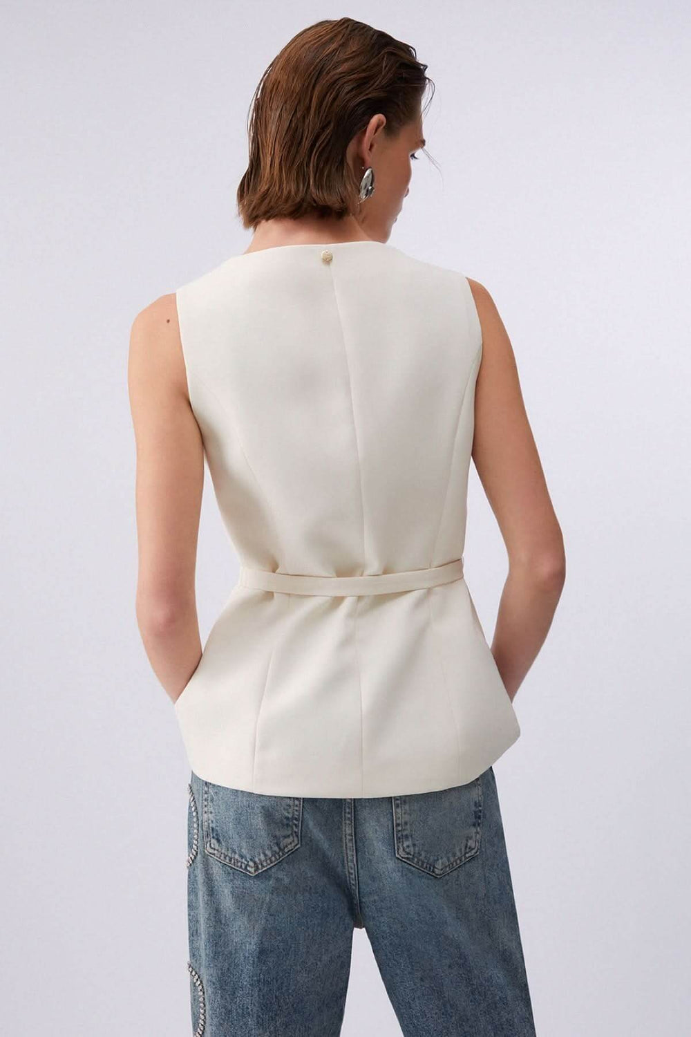 Femme portant une veste sans manches avec ceinture, vue de dos, mettant en valeur la coupe structurée.