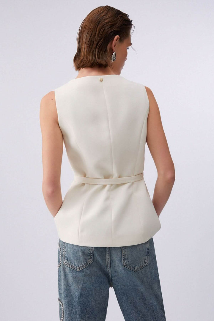 Femme portant une veste sans manches avec ceinture, vue de dos, mettant en valeur la coupe structurée.