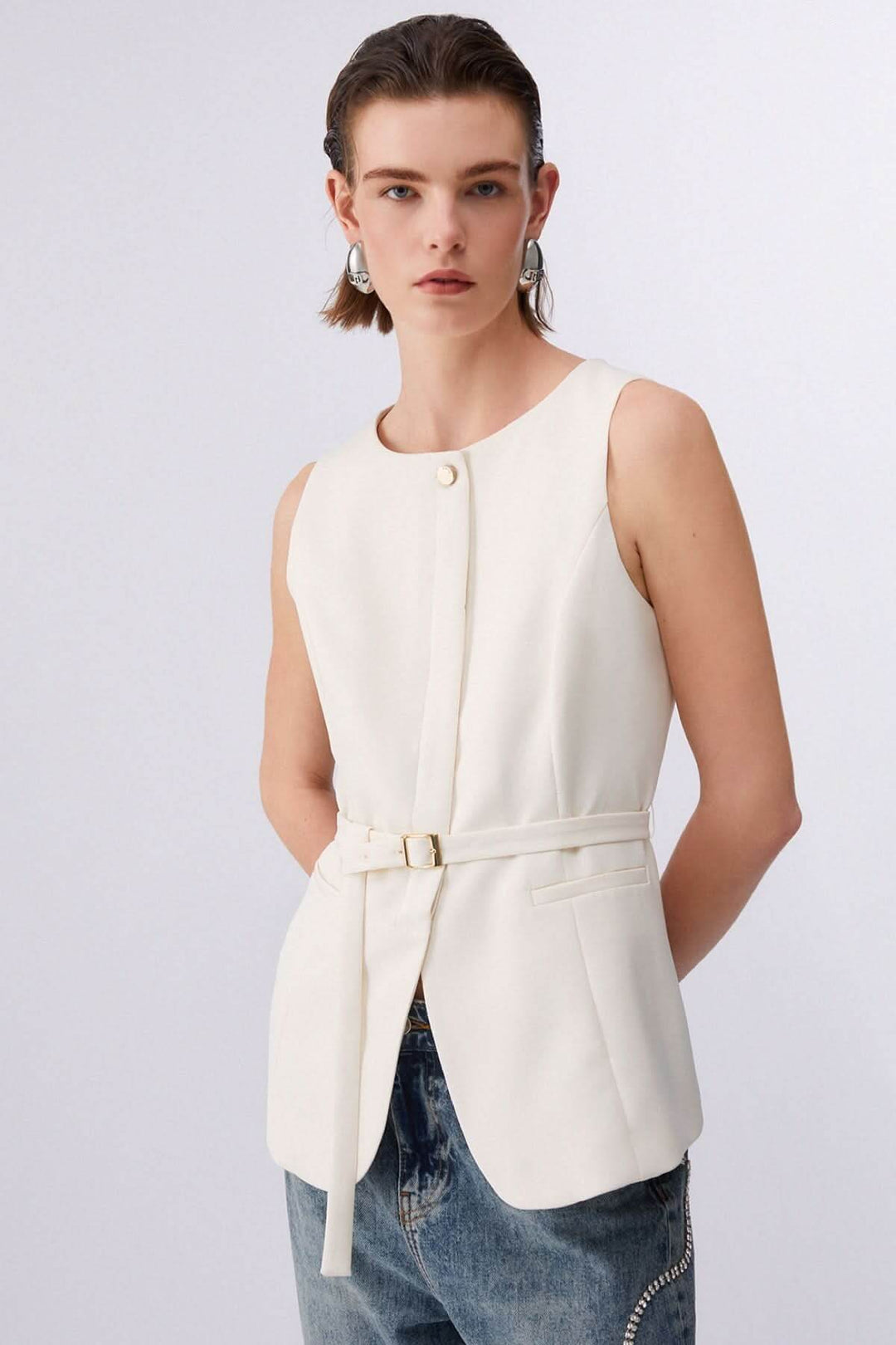 Femme portant une veste sans manches avec ceinture ajustable, élégante et structurée, sur chemise et jean décontracté.