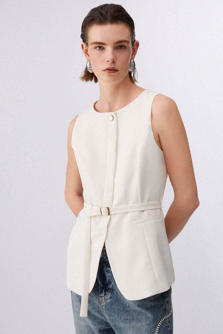 Femme portant une veste sans manches avec ceinture ajustable, élégante et structurée, sur chemise et jean décontracté.