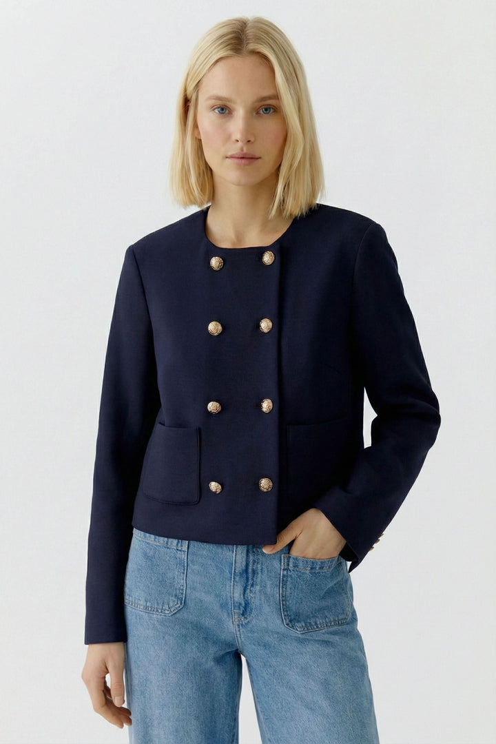 Femme portant une veste structurée à boutons décoratifs, style élégant et sophistiqué, idéale pour rehausser un denim ou un look habillé.