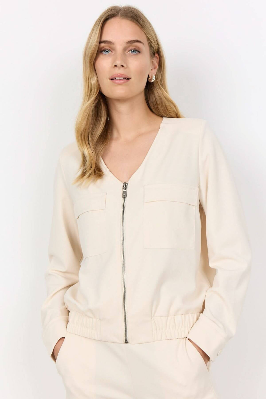 Veste zipée crème avec col en V, poches plaquées et ourlet élastique, idéale pour tenues décontractées.