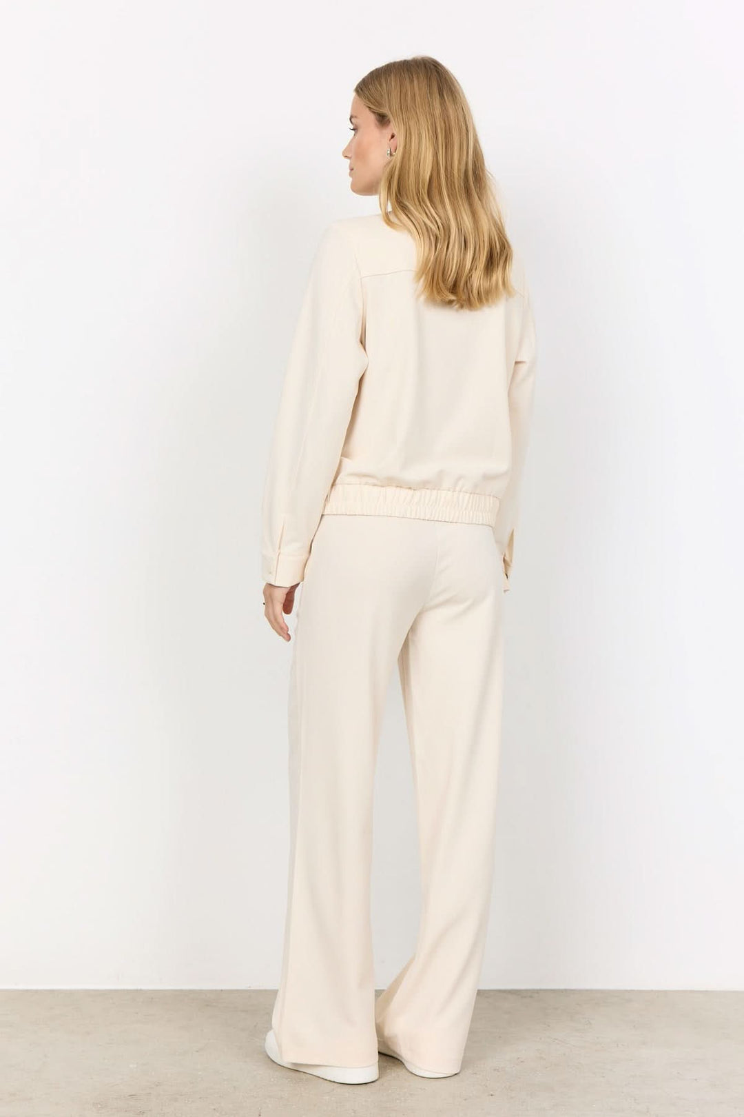 Femme vue de dos en tenue décontractée beige avec pantalon large et sweat-shirt, style confortable et élégant.