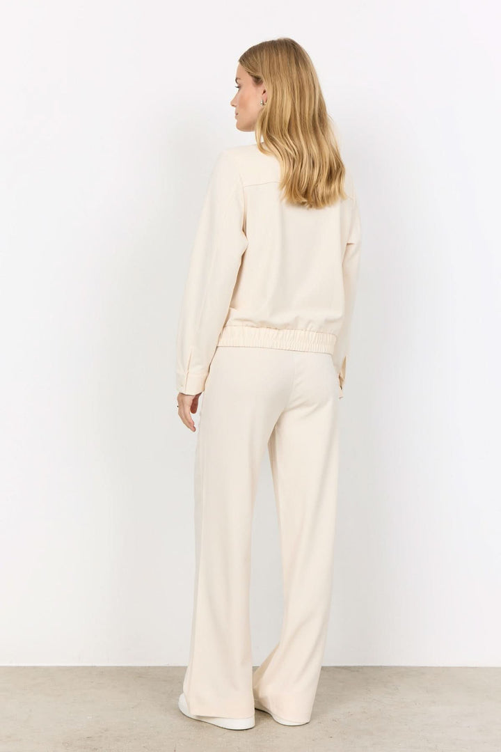 Femme vue de dos en tenue décontractée beige avec pantalon large et sweat-shirt, style confortable et élégant.
