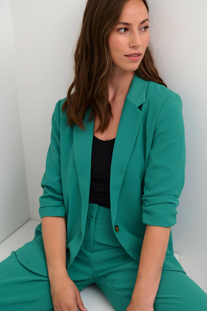 Femme portant un veston cocamia turquoise avec un top noir, style décontracté et professionnel.