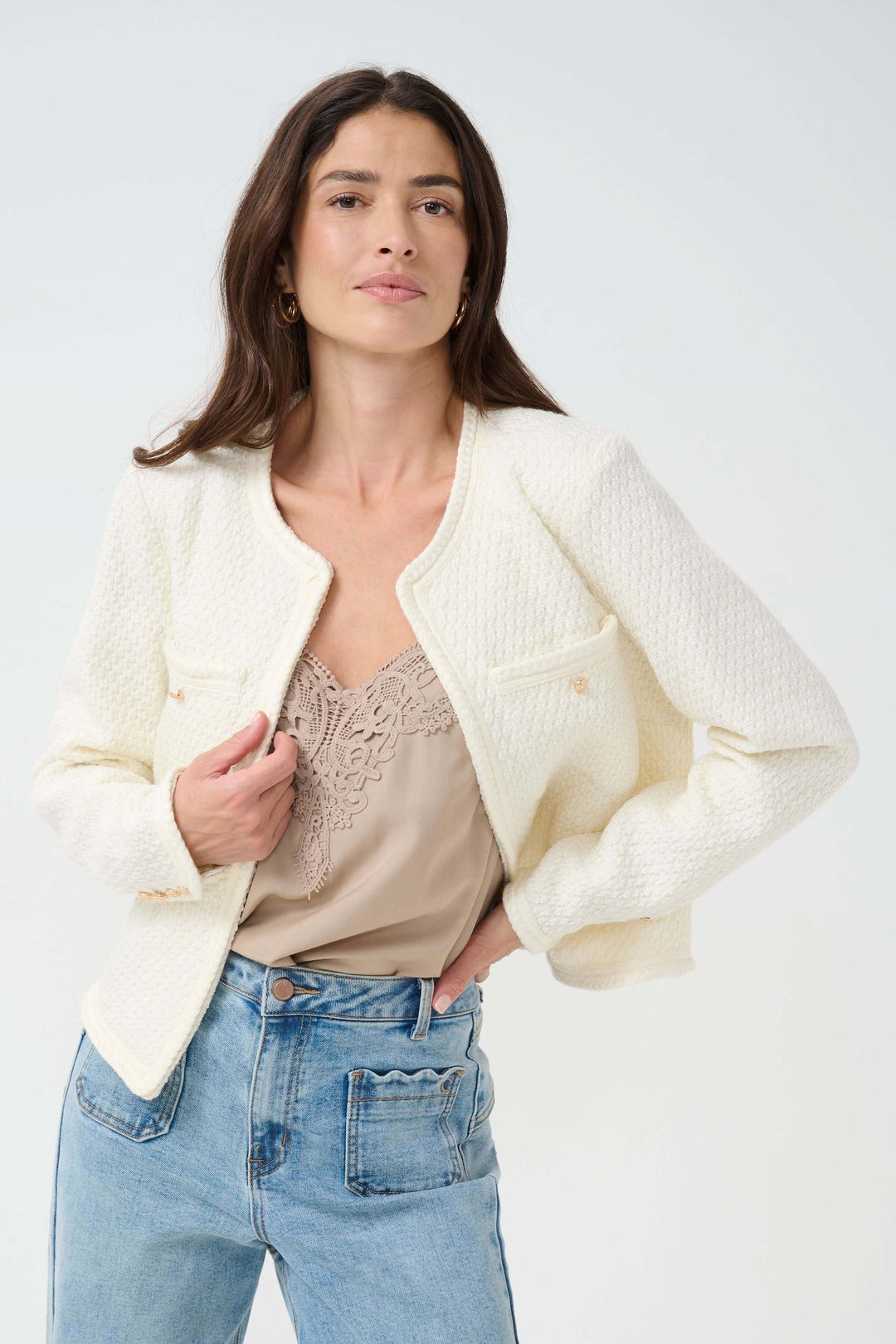 Veston Janiah en tissu bouclé, coupe courte, élégant et féminin, associé à un débardeur beige et jeans.