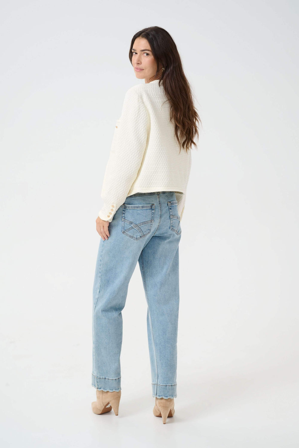 Femme portant un veston structuré écru, jean décontracté et talons, vue de dos.