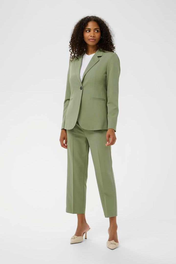 Veston à coupe droite vert, avec col tailleur classique et fermeture épurée, porté par une femme pour un look professionnel et élégant.