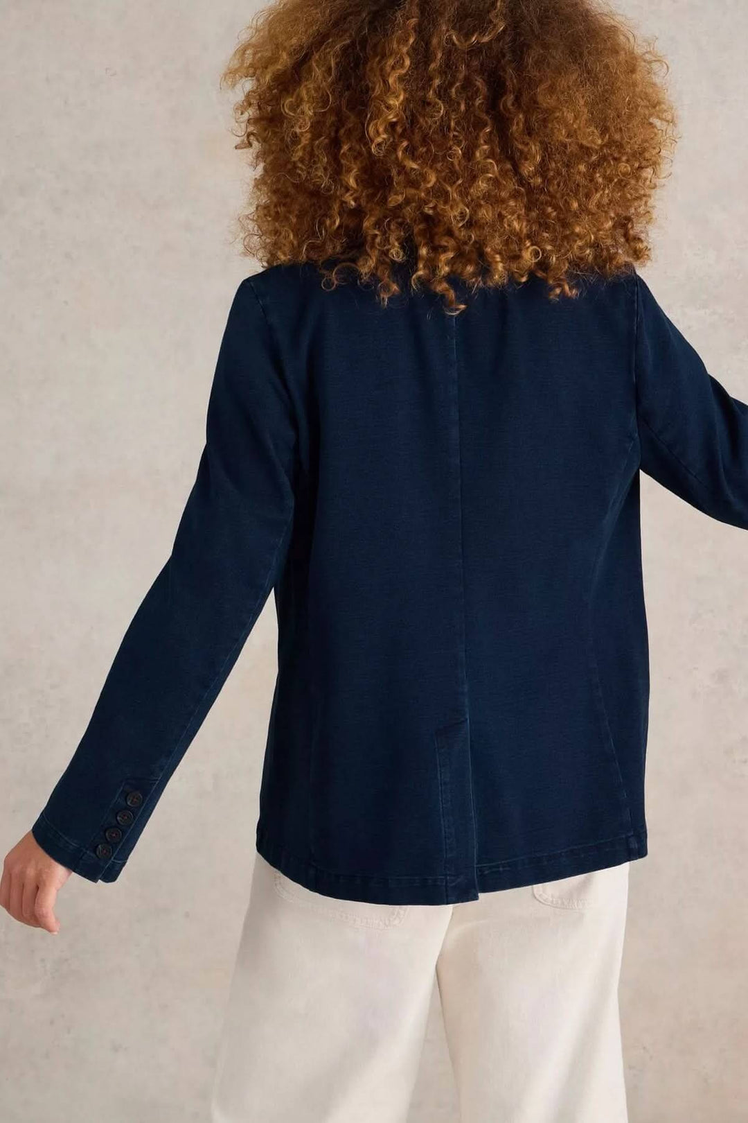 Veston décontracté en denim bleu marine, coupe droite, vu de dos avec cheveux bouclés en arrière.