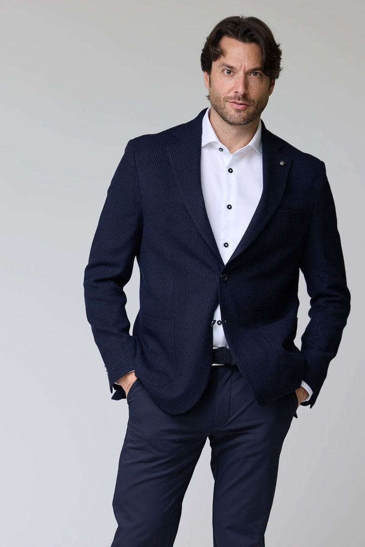 Homme portant un veston en tricot structuré bleu, élégant et confortable, avec chemise blanche, pour un style raffiné.