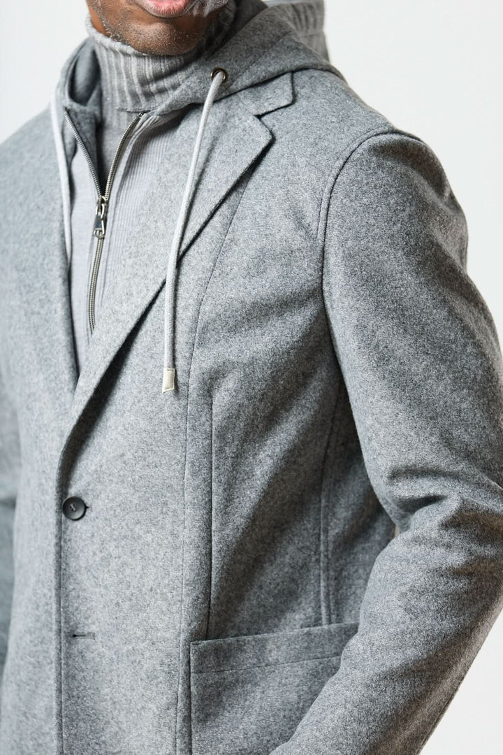 Veston hybride à capuche gris avec capuche à cordons, porté sur un col roulé en laine fouillée, style urbain élégant.