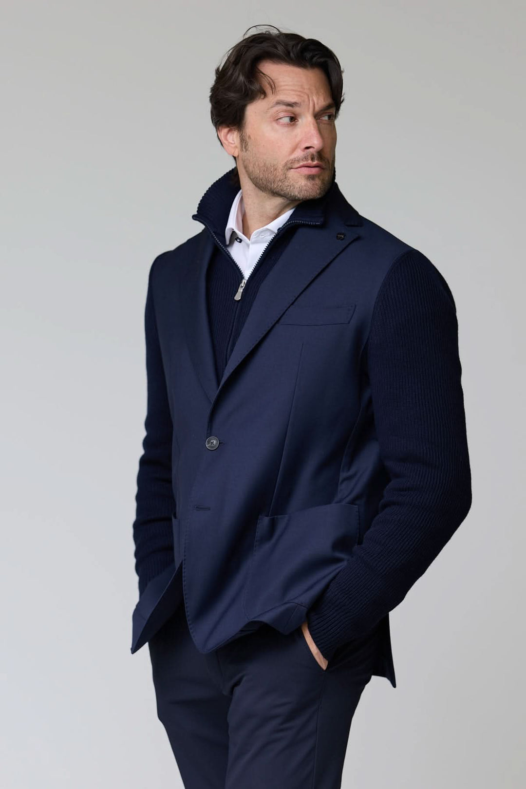 Homme portant un veston hybride tricot et tissu bleu avec manches en maille et fermeture à deux boutons, col à revers classique.