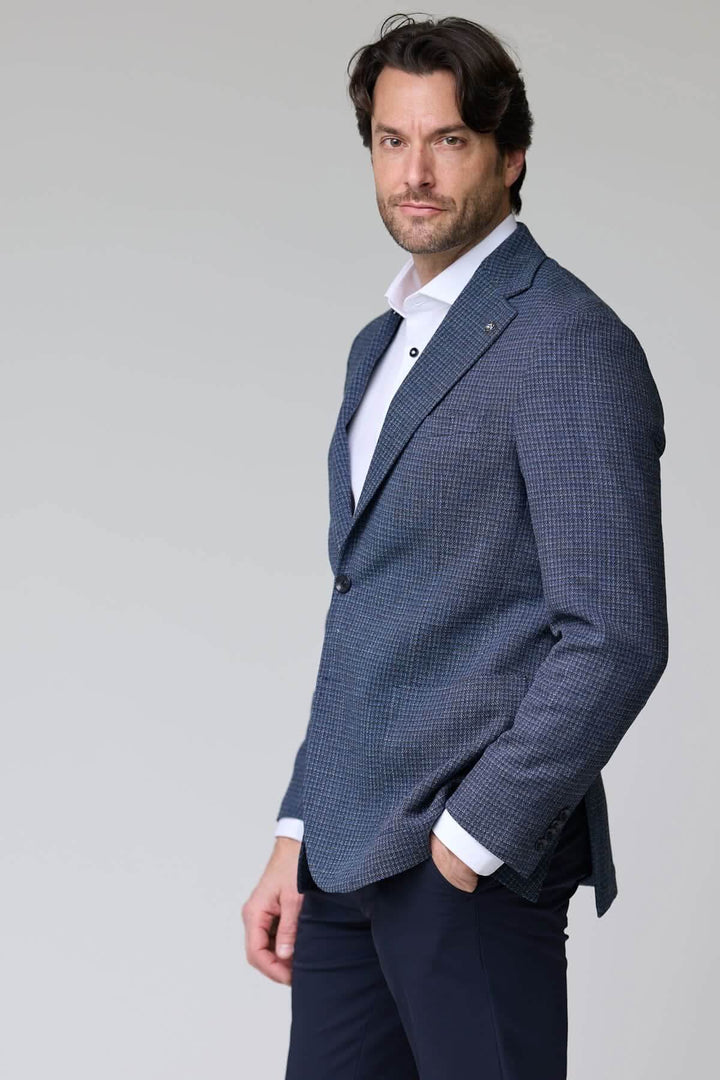 Homme portant un veston à motif texturé, bleu, avec col à revers. Parfait pour l'élégance moderne au bureau ou en événement formel.