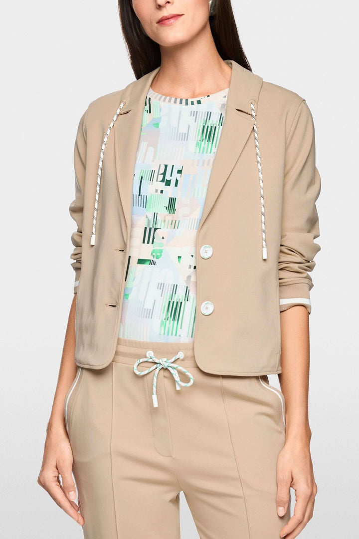 Veston sportif à détails rayés avec capuchon intégré en tissu beige, porté sur un t-shirt graphique coloré.