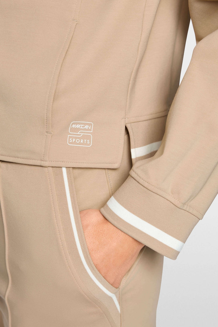 Veston sportif à détails rayés beige avec capuchon intégré, coupe courte et structurée, détail de poignet rayé.