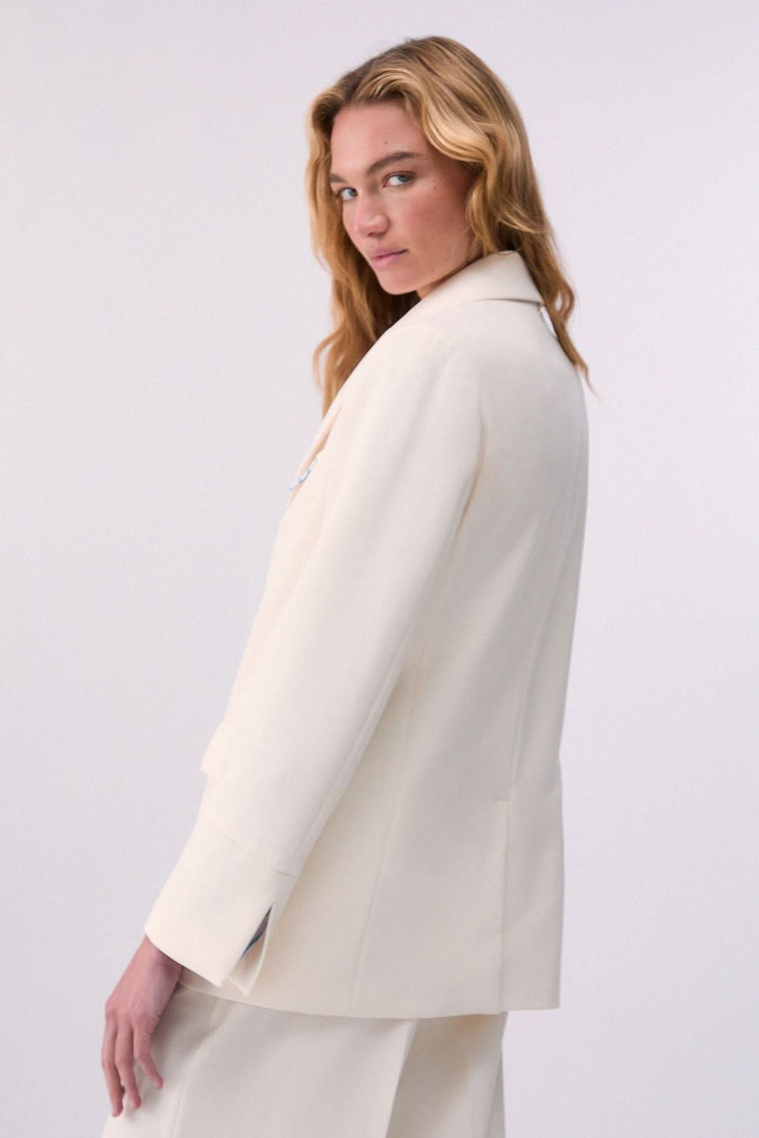 Veston structuré à coupe ajustée en tissu blanc, porté par un modèle, montrant la coupe élégante et le col tailleur classique.