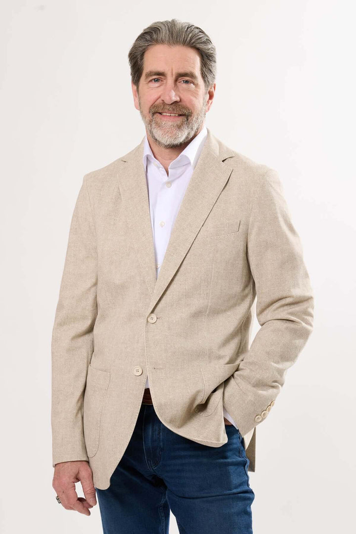 Homme souriant portant un veston beige léger, chic décontracté, idéal pour les journées estivales.