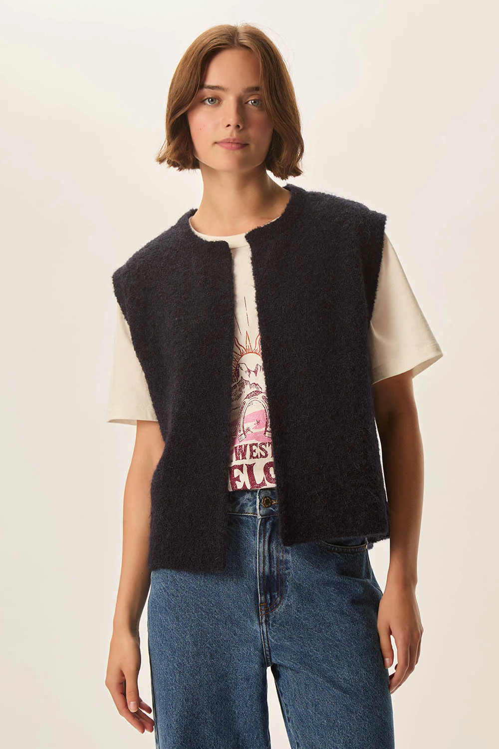 Femme portant une Veste Achille sans manches en laine bouclée, style décontracté avec jean et t-shirt imprimé.