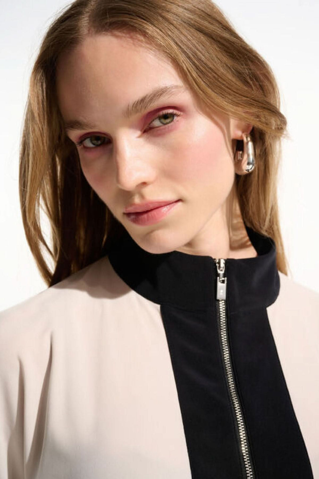 Haut à col zippé structuré en tissu fluide avec col montant et fermeture éclair, moderne et épuré, porté par une femme.