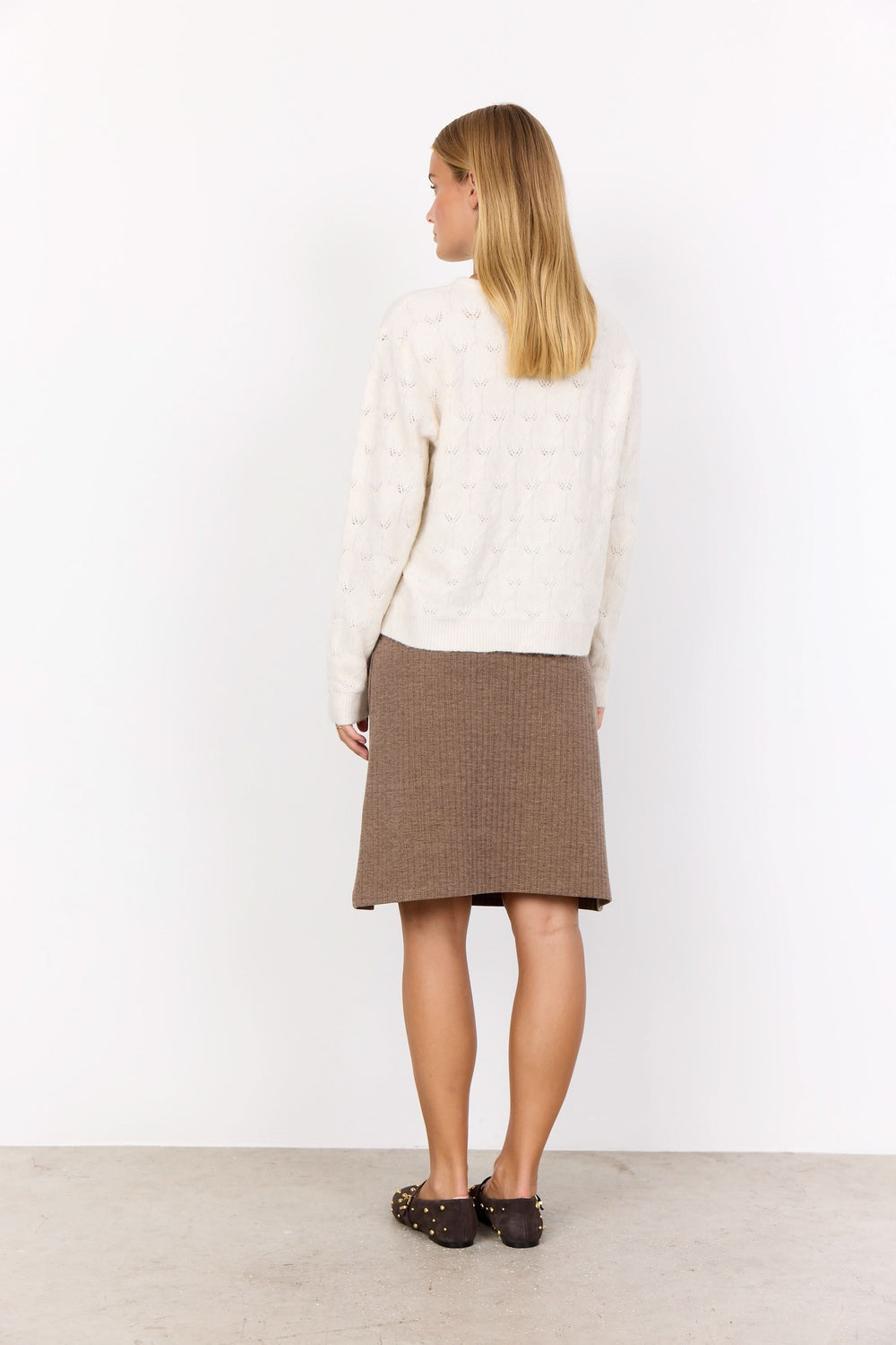 Femme vue de dos portant un cardigan crème avec une jupe en tricot marron, style cosy et élégant.