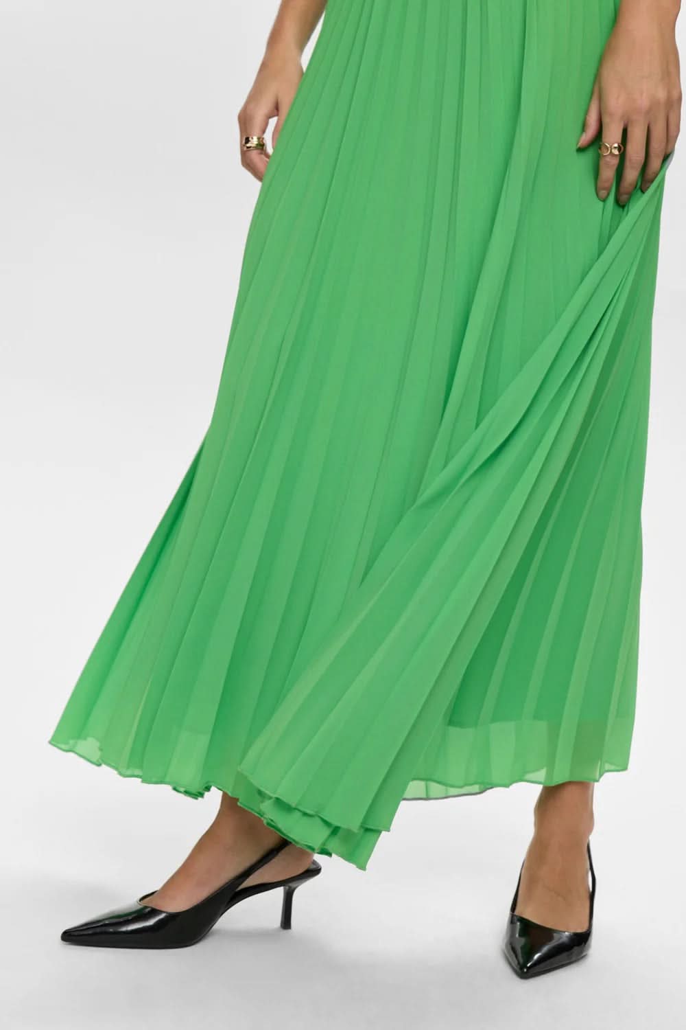 Jupe longue plissée à fines bretelles en tissu léger vert, offrant une silhouette élégante et fluide avec détails de plis raffinés.